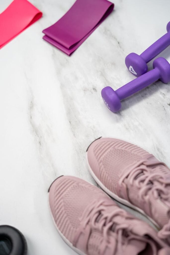 Flat lay of pastel pink fitness gear including sneakers and dumbbells on marble texture.